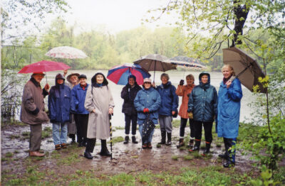 photo of club members touring Black Nook in 2023 during a rain storm; they are smiling, wearing raincoats and holding umbrellas