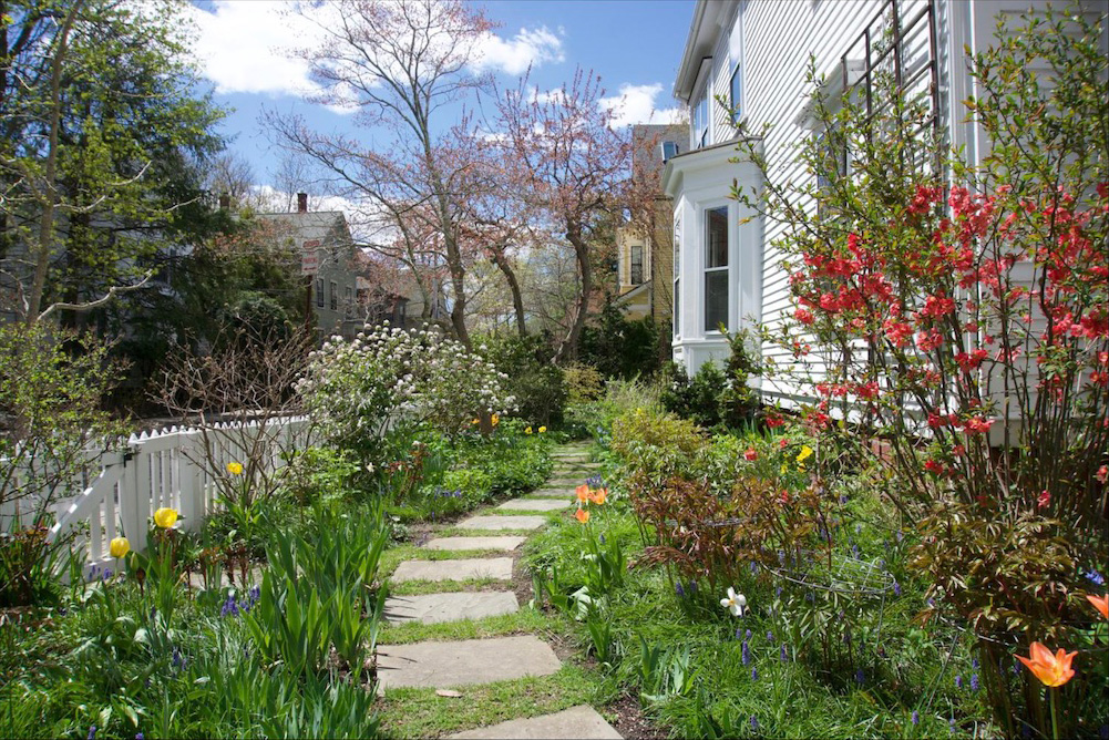 Photo of a home garden with flowers, stone path, and white picket fence.
